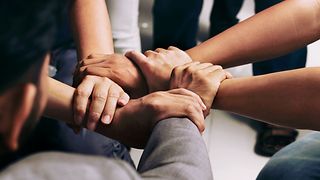 Five interlocking hands of different colleagues in a circle, viewed from above