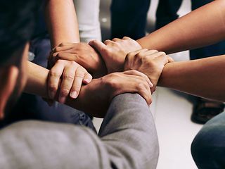 Five interlocking hands of different colleagues in a circle, viewed from above