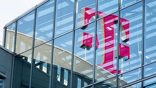 Das große rote Telekom Logo spiegelt sich in der Glasfassade eines modernen Gebäudes