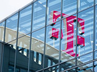 Das große rote Telekom Logo spiegelt sich in der Glasfassade eines modernen Gebäudes