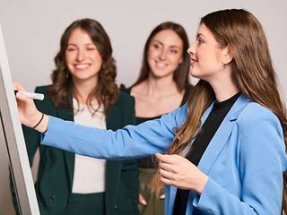  Eine Gruppe von drei Frauen arbeitet interaktiv an einem Flipchart. 