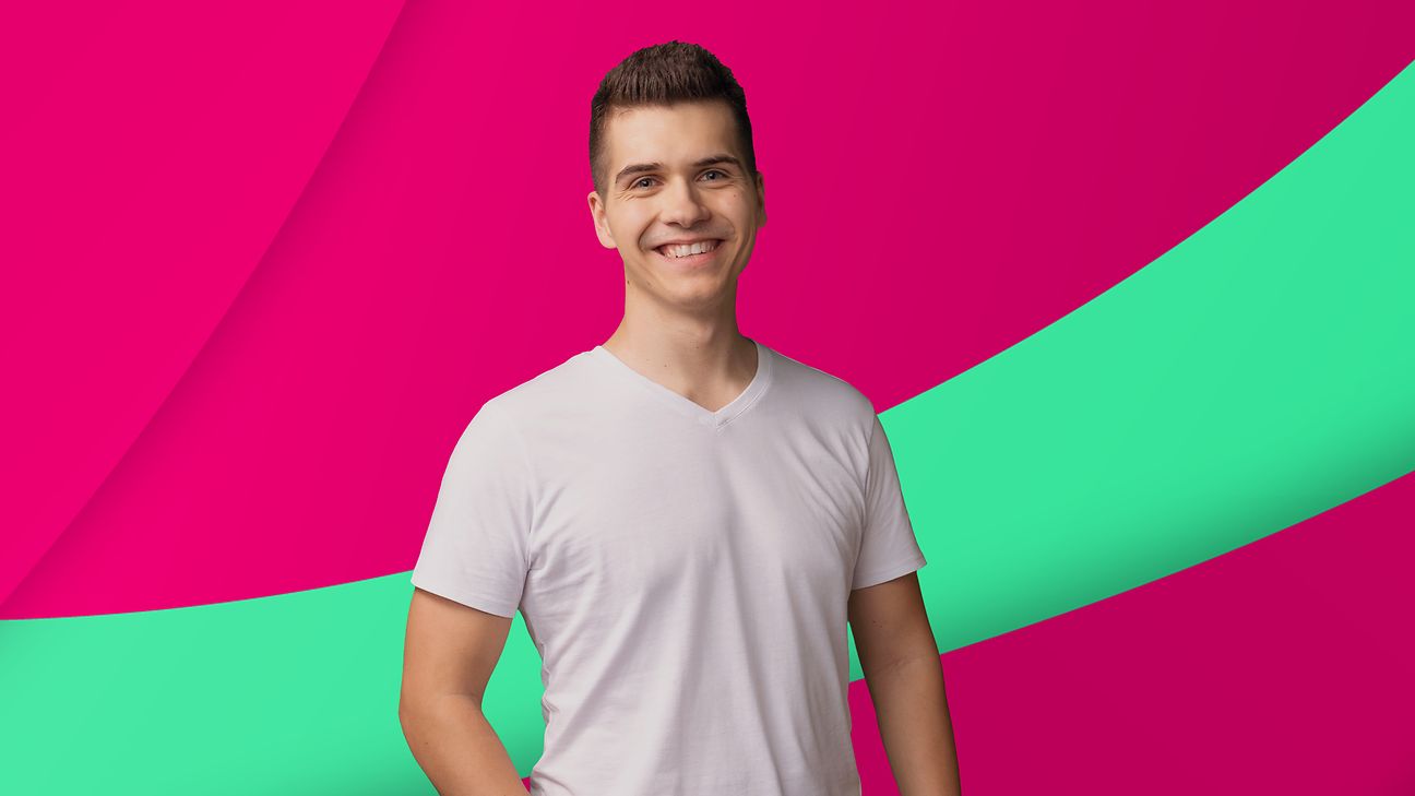 Junger Mann schaut fröhlich und offen in die Kamera während er vor einem magenta-farbenen Hintergrund steht.