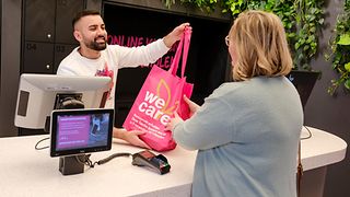 A salesperson passes a shopping bag over the counter to a woman in the Telekom shop