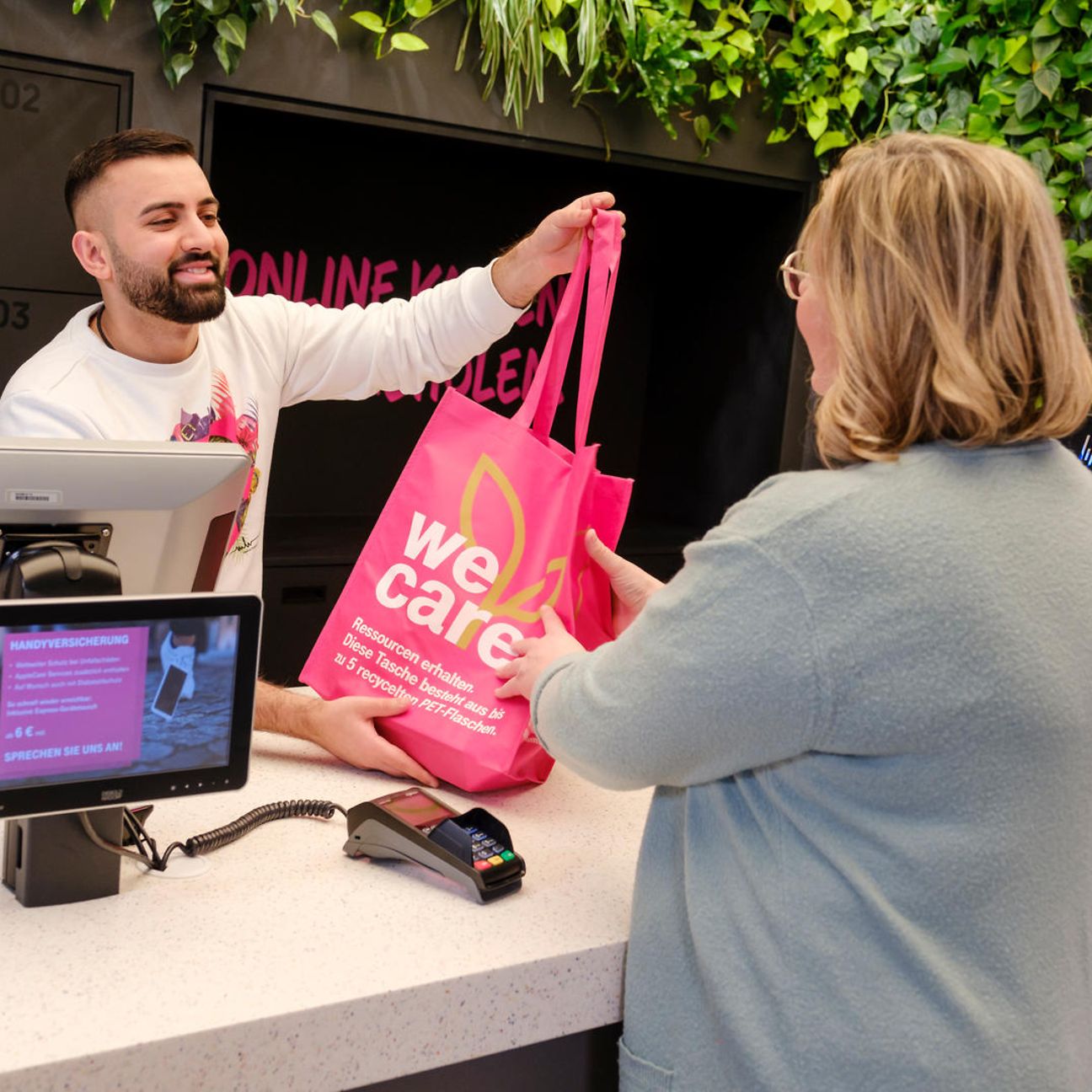 A salesperson passes a shopping bag over the counter to a woman in the Telekom shop