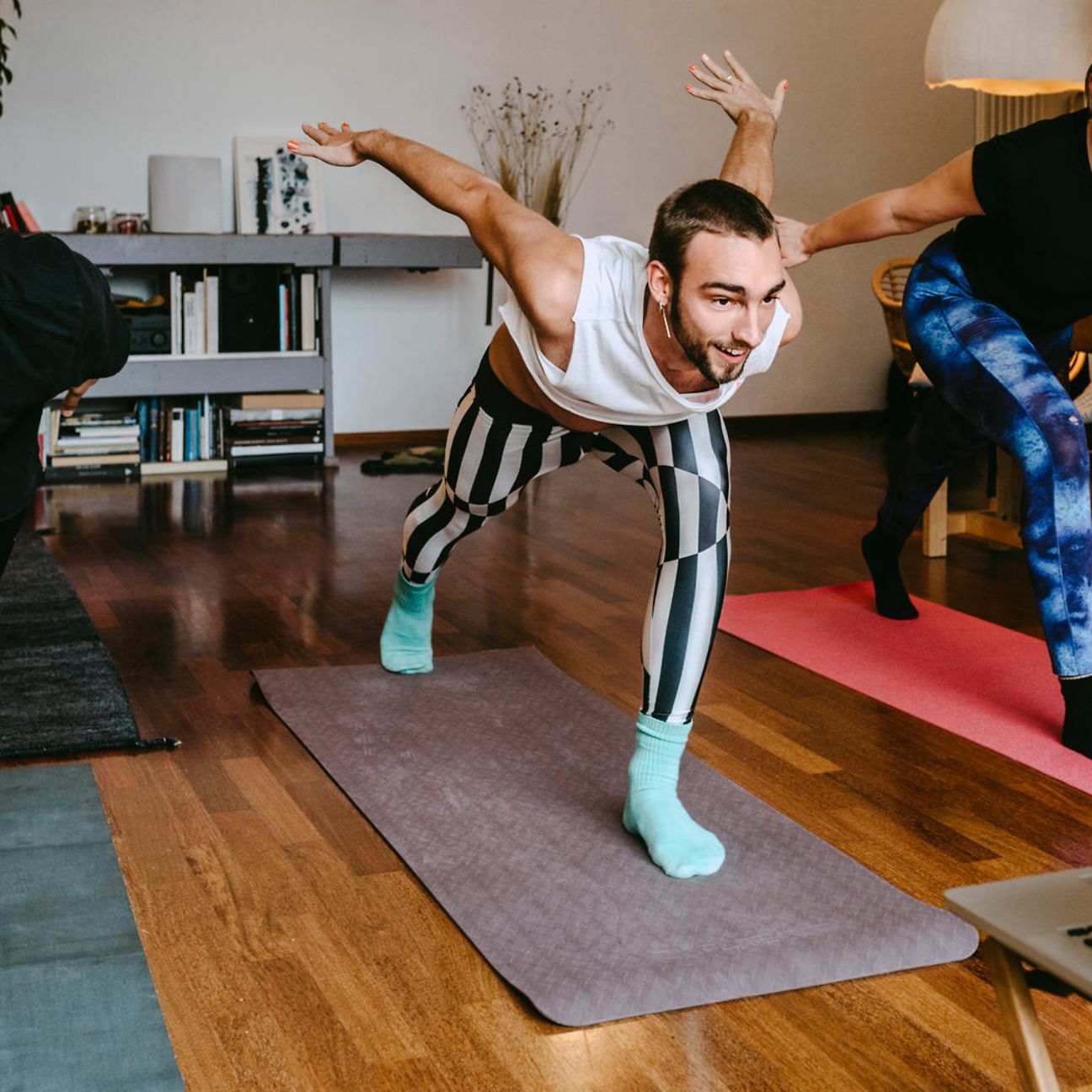 Three people in a good mood do a balance exercise on yoga mats.