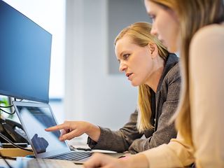 A woman explains something to another on a laptop in an office