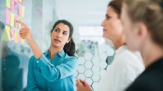 Group of three women standing and talking in front of a pinboard with many post-its