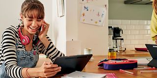 Young woman makes a phone call using a smartphone while looking at a tablet.