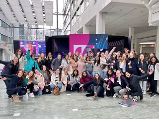 A large group of women looks into the camera, smiling and cheering.