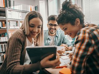 Young people sit happily together and work together on the tablet.