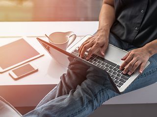 Man sitting on window sill, working at his laptop.