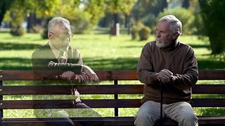 A real and a virtual man talking while sitting on a bench.