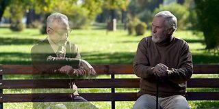 A real and a virtual man talking while sitting on a bench.