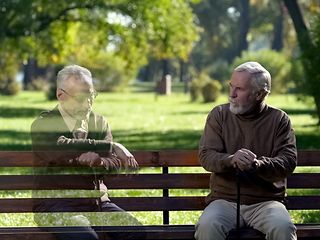 A real and a virtual man talking while sitting on a bench.