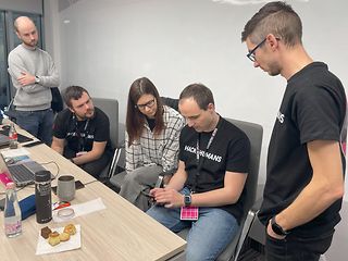 A man shows an application on his cell phone, two other men and a woman watch.