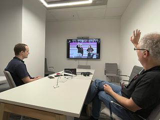 Two men at a table in front of a large screen.