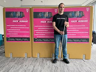 Man with a cane in front of posters with the inscription “Hack4Humans 2024”