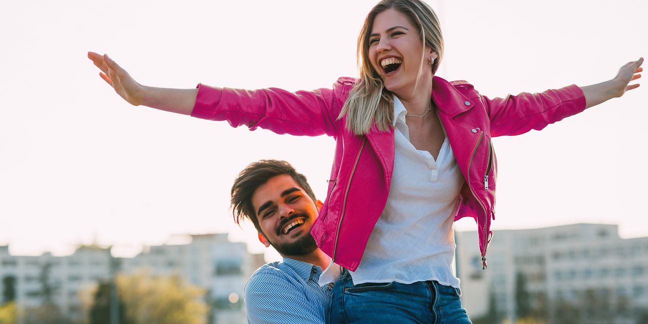 A man lifts his partner up. She stretches her arms wide open upwards.