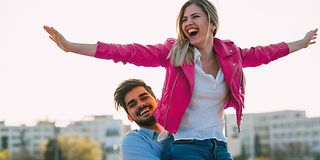 A man lifts his partner up. She stretches her arms wide open upwards.