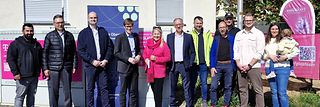 Die Teilnehmenden stehen an der Straßenecke vor einem Verteilerkasten. Im Hintergrund Banner von Telekom und Zweckverband. 