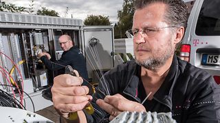 Zwei Techniker arbeiten am Ausbau des Breitbandnetzes. Ein Techniker kürzt mit einer Zange einzelne Glasfasern ein. 