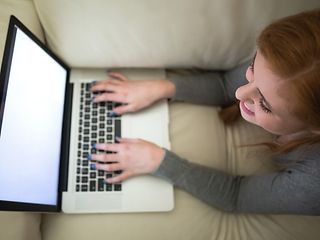Junge Frau liegt mit Laptop auf Sofa