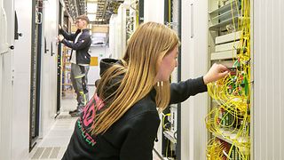 Eine junge Frau sitzt in der Hocke und untersucht einen Netzwerkschrank.