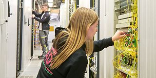 Eine junge Frau sitzt in der Hocke und untersucht einen Netzwerkschrank.