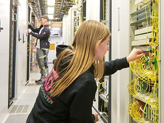 Eine junge Frau sitzt in der Hocke und untersucht einen Netzwerkschrank.