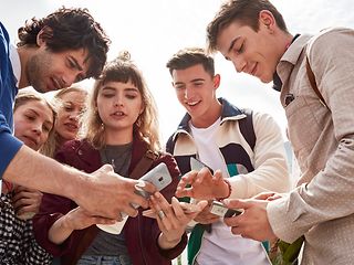 Young people standing in a circle holding the smartphones in the middle, discussing the contents