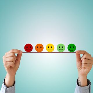 Zwei Hände halten eine fünfstufige Smiley-Skala hoch