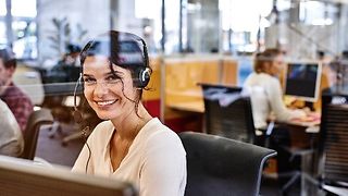 Woman sits in the office wearing a headset.