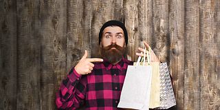 Young man with a beard pointing at shopping bags.