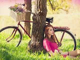Frau und Fahrrad mit Einkaufskorb lehnen an einem Baum.