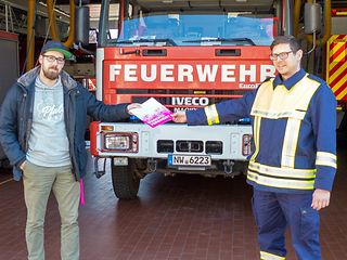 Shopleiter Rene Werling überreicht Feuerwehrmann Timo Krämer vor der Fahrzeughalle der Leitstelle die SIM-Karten.