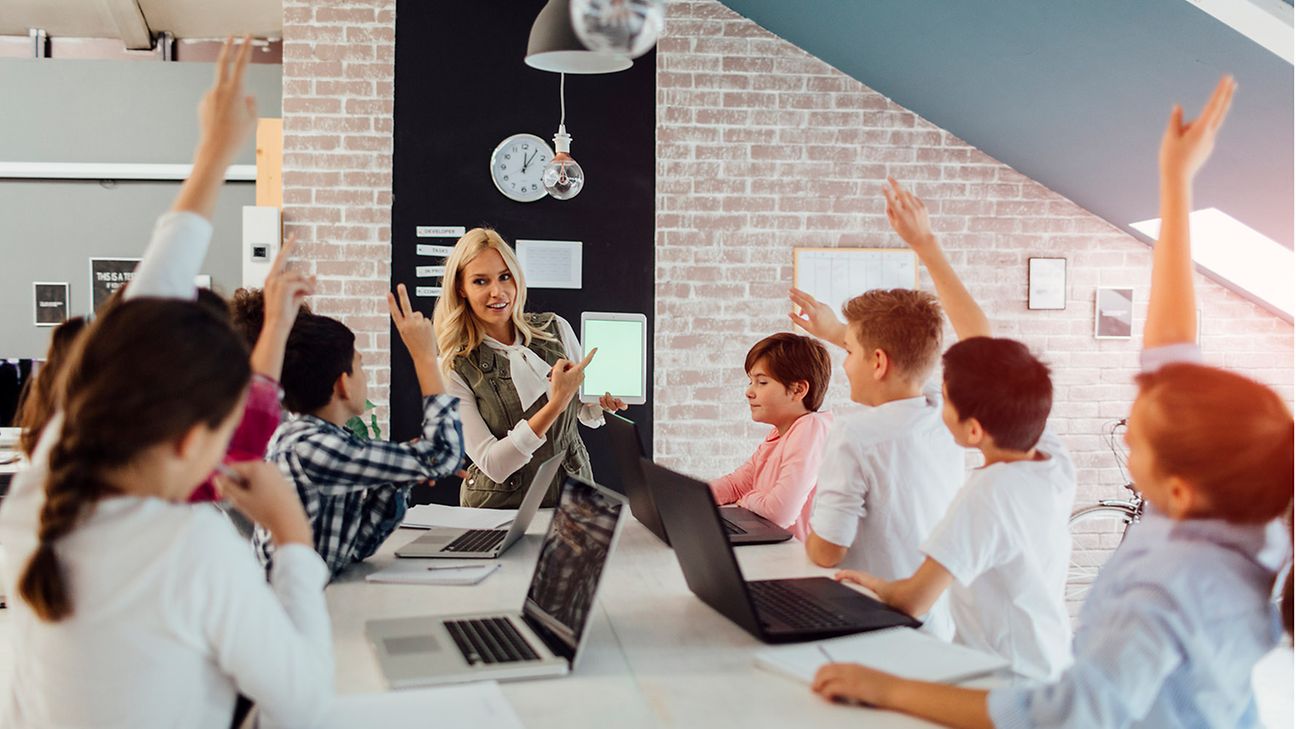 Schüler*innen sitzen mit Lehrerin am Tisch mit Laptops vor sich.