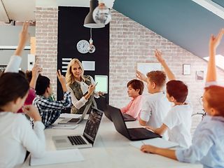 Schüler*innen sitzen mit Lehrerin am Tisch mit Laptops vor sich.